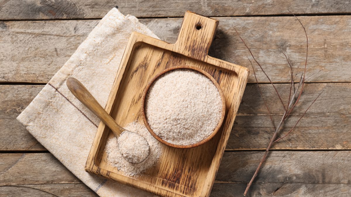 psyllium husk in a bowl and spoon on a wooden tray on a wooden table with a branch next to it