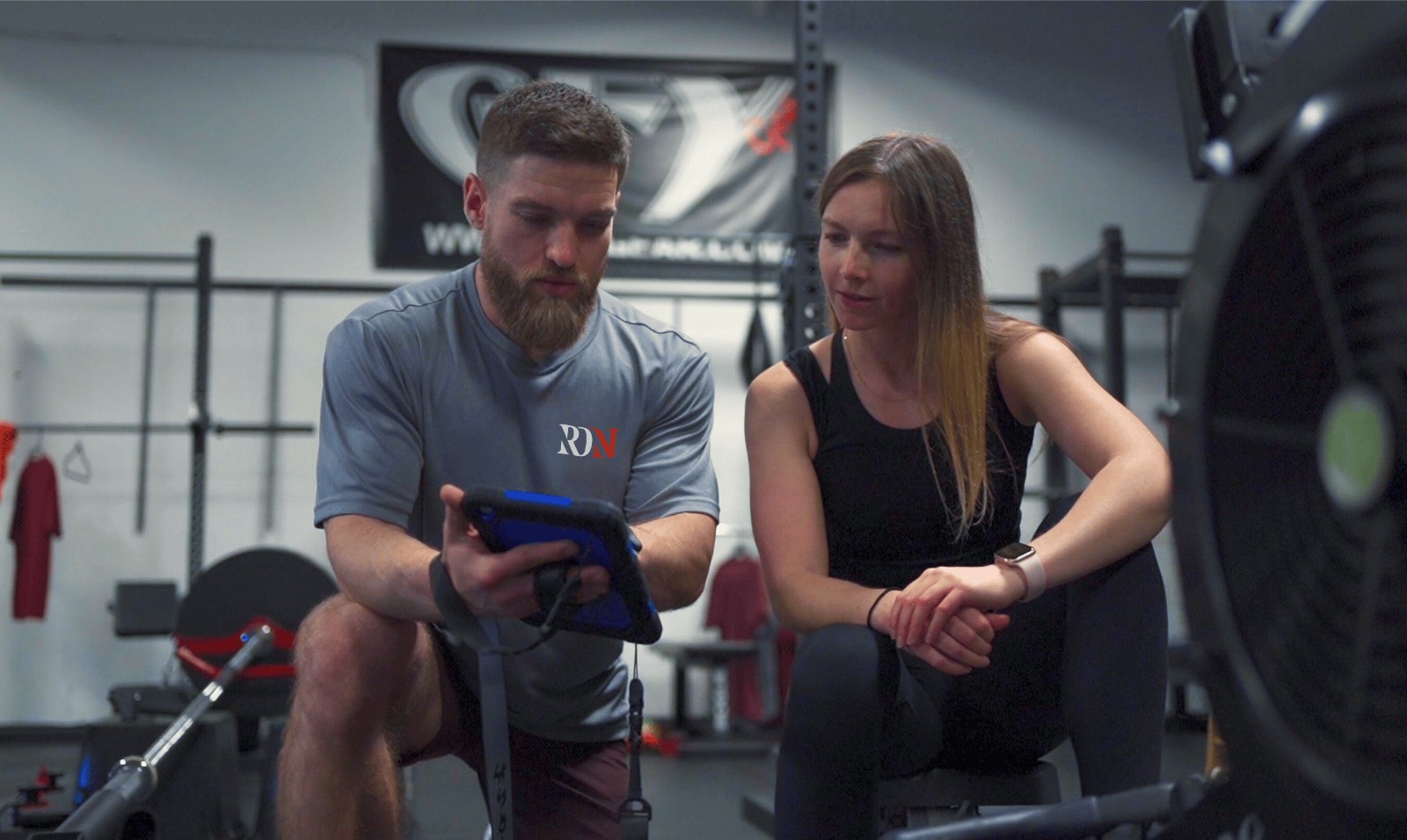 Kevin Rogers reviewing a client's training data with her on a tablet in the gym